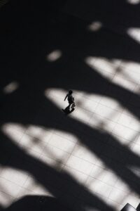 Person walking down broad corridor with shadows of individual and building structure visible representing institutional repression